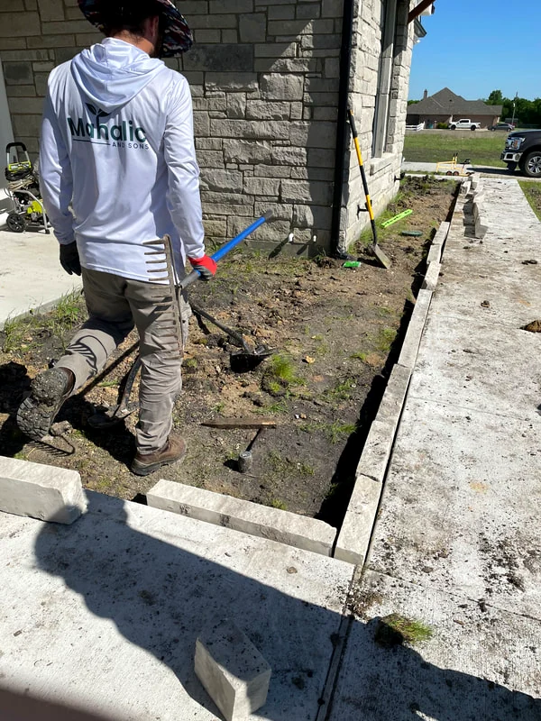 Mahalic and Sons crew member blowing clippings off a driveway after mowing